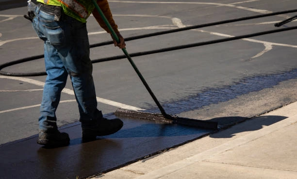 Worker applying bitumen coating during road surface repair as part of road construction materials process.