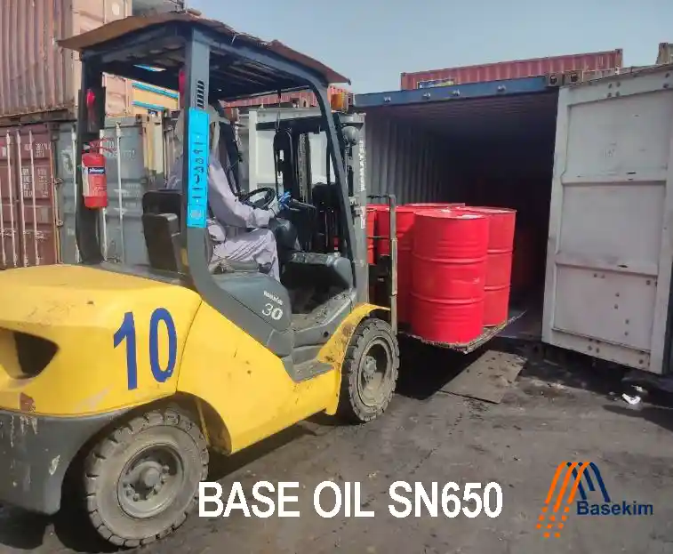 Forklift loading red drums of BASEOIL SN 650 into a shipping container at Basekim’s warehouse.