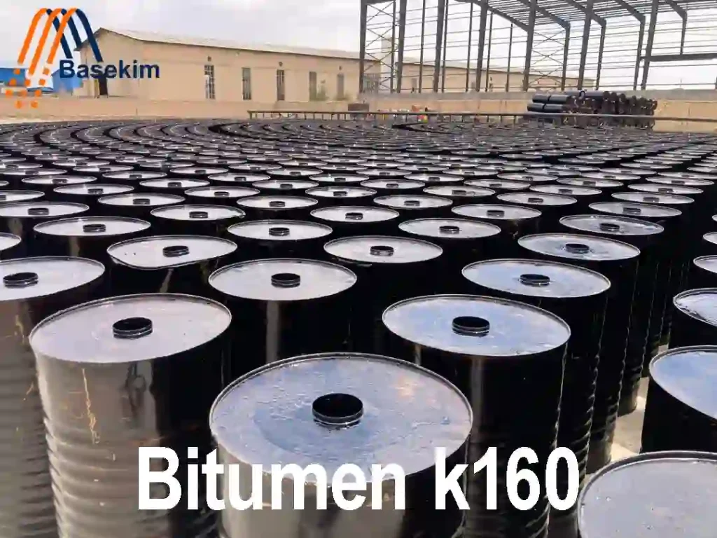 Large stock of sealed black steel drums filled with Bitumen K160, stored under a covered yard with Basekim branding visible.