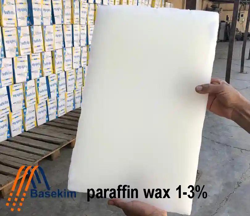 Large white slab of paraffin wax 1-3% held by hand in front of stacked Basekim cartons, ready for export.
